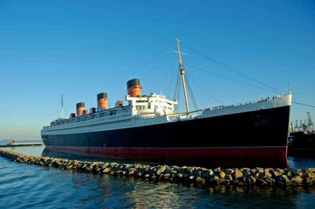black, white and red queen mary ship docked in the water surrounded by a rock wall