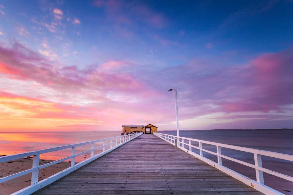 a long wooden pier with a yellow building at the end at sunset