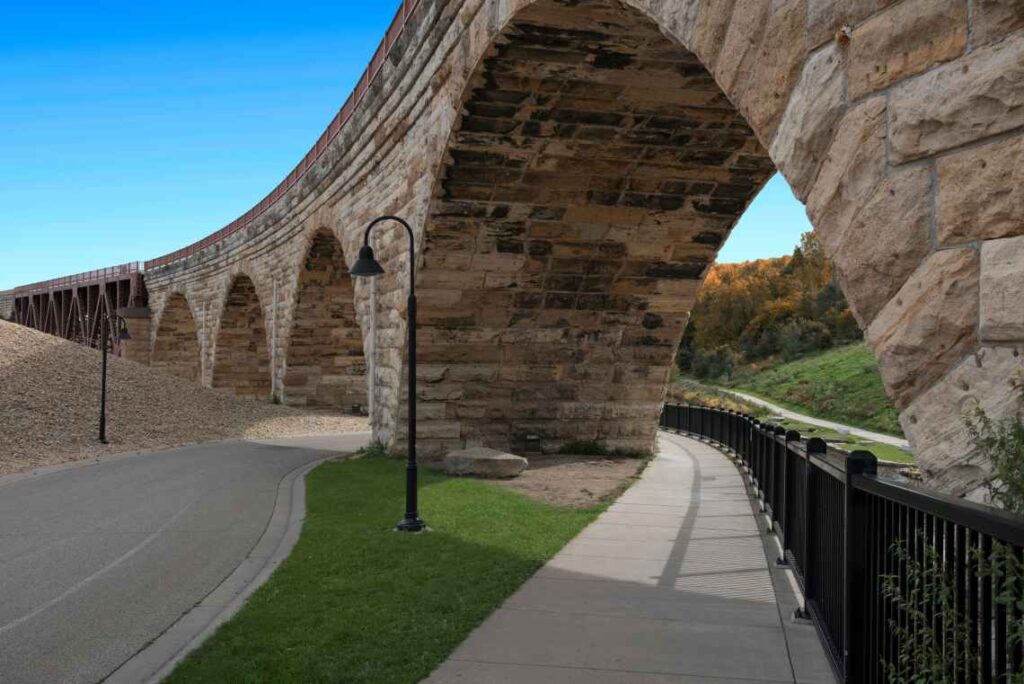 paved bike path sidewalk under bridge made of stone with arches on a sunny day