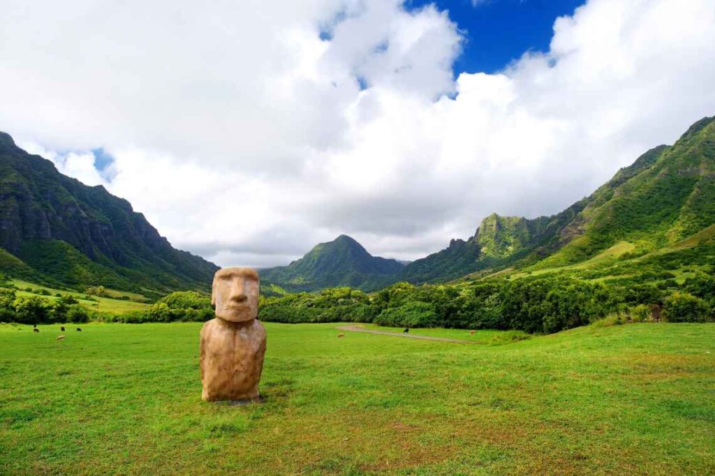 brown easter island head statue sitting in a lush green valley surrounded by green mountains on kualoa ranch