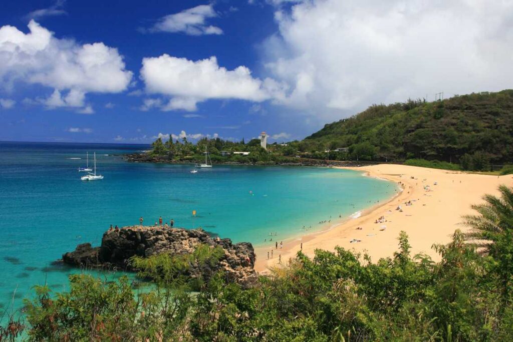 wide beach on oahu's waimea bay with boats on the turquoise water and green mountains rising on either side
