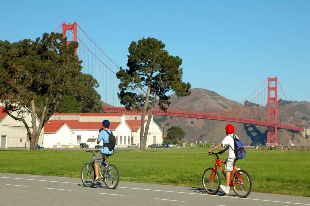 2 people riding bikes on a paved bike path with the golden gate bridge in the background