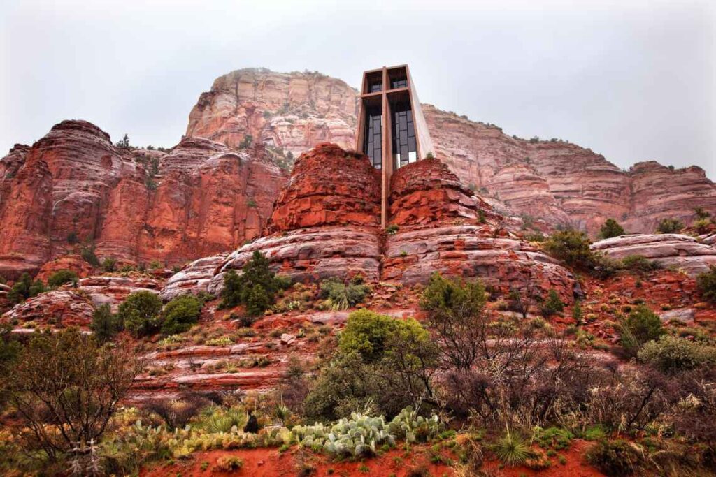 glass chapel with a cross rising from the red rocks outside of sedona on a gray day