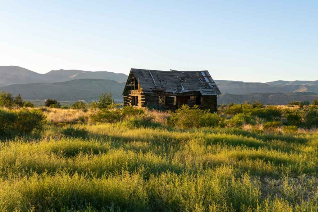 falling apart wooden building sitting amid grass in front of mountains