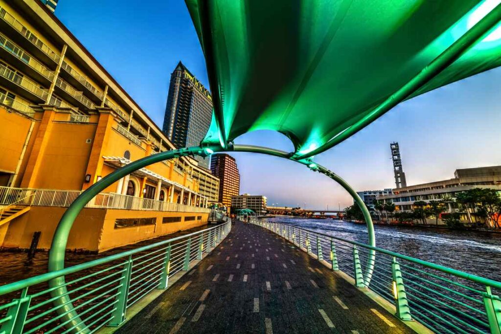 black stone walkway by the water with an orange stone building to the left and a green walkway and railings above