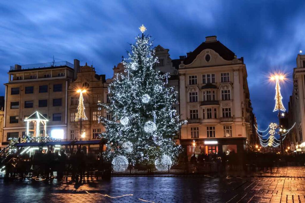 large christmas tree with white lights on a plaza with christmas market stalls