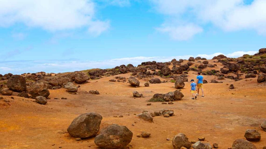 Mountain of red dirt and rocks with man and child wearing yellow shorts and blue t-shirt.