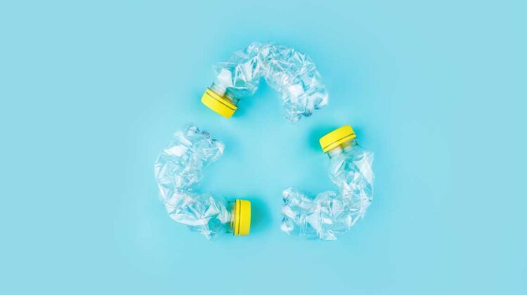 crushed plastic bottles in a recycling symbol triangle against a blue-green background