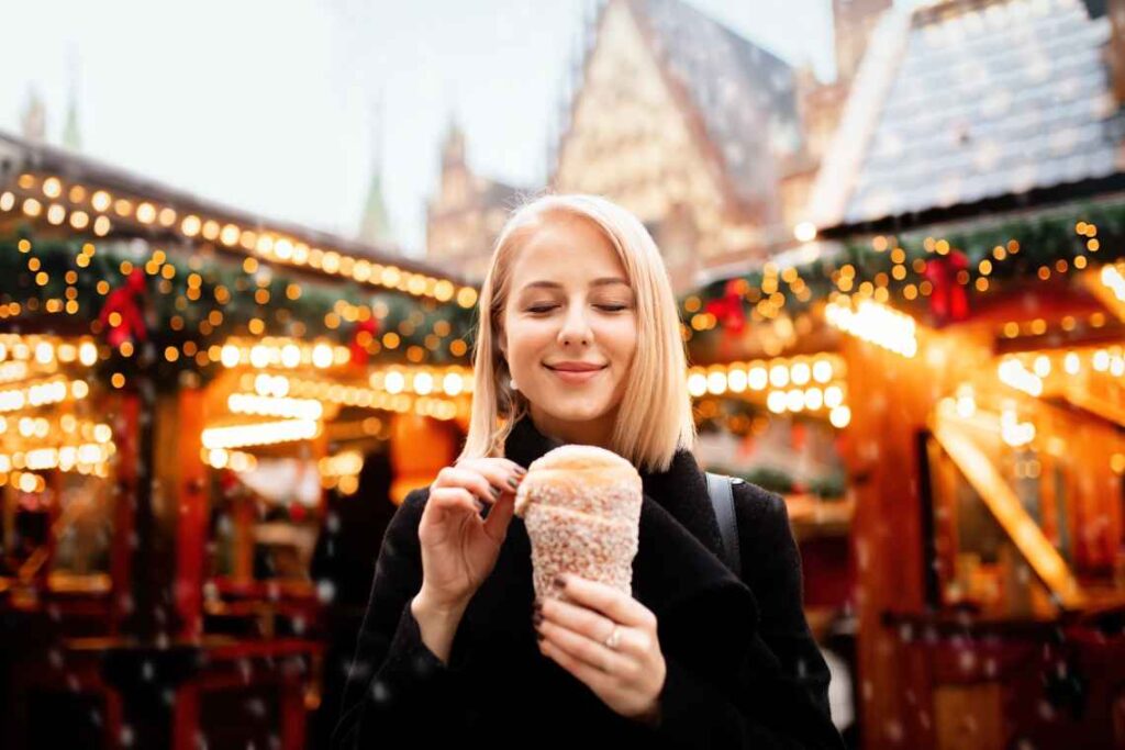 blond woman in a black coat eating a polish pastry in a christmas market in wroclaw