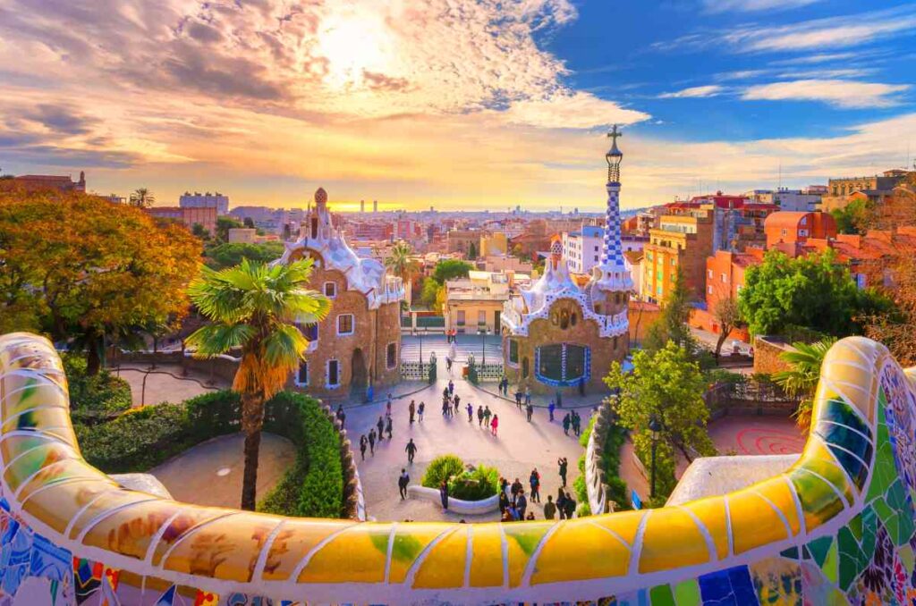 brightly colored curving wall and houses from the artist gaudi in barcelona, spain at sunset