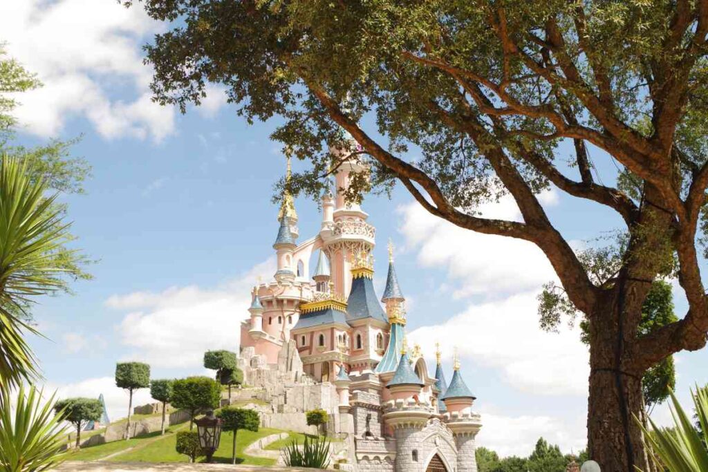The pink and blue castle with a stone base and turrets at disneyland paris on a sunny day