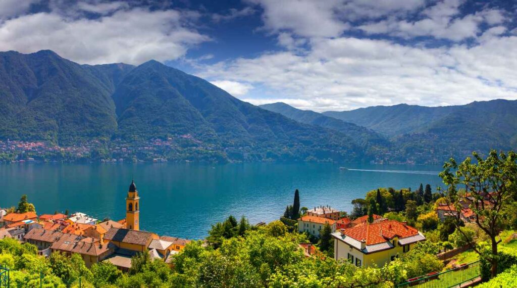 overhead shot of steep green mountains surrounding lake como italy with a town below