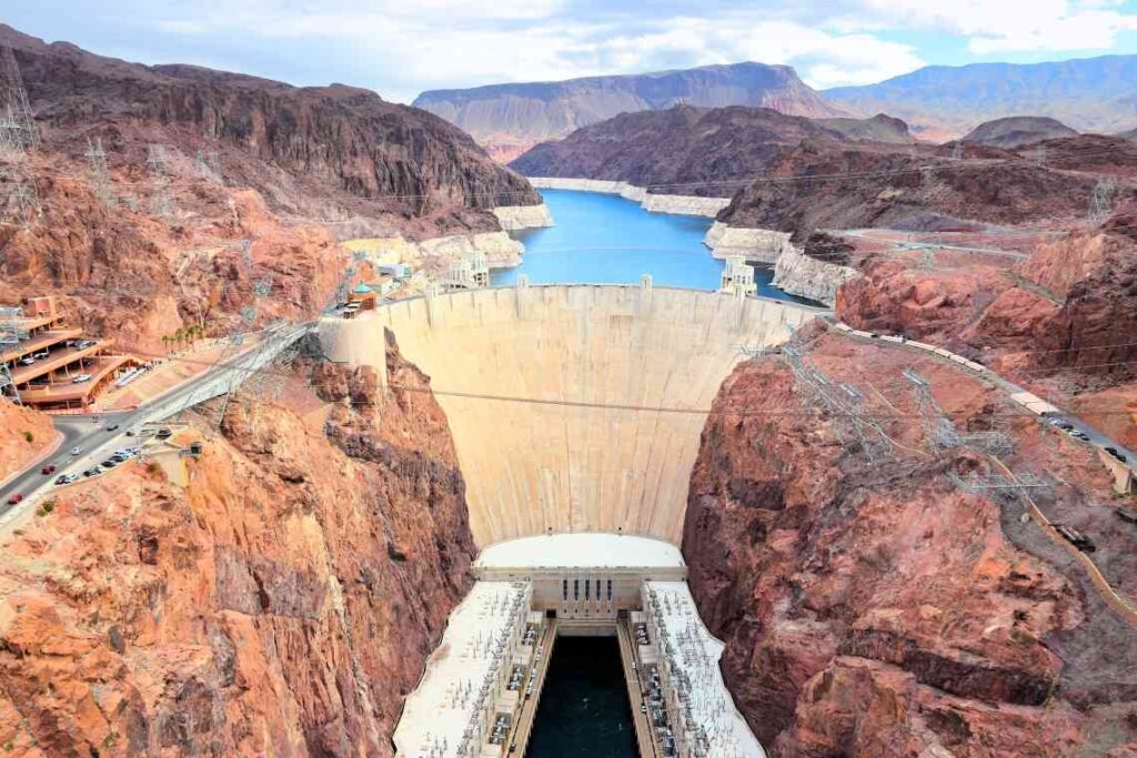 view of the hoover dam from above with red rocks and blue water behind it