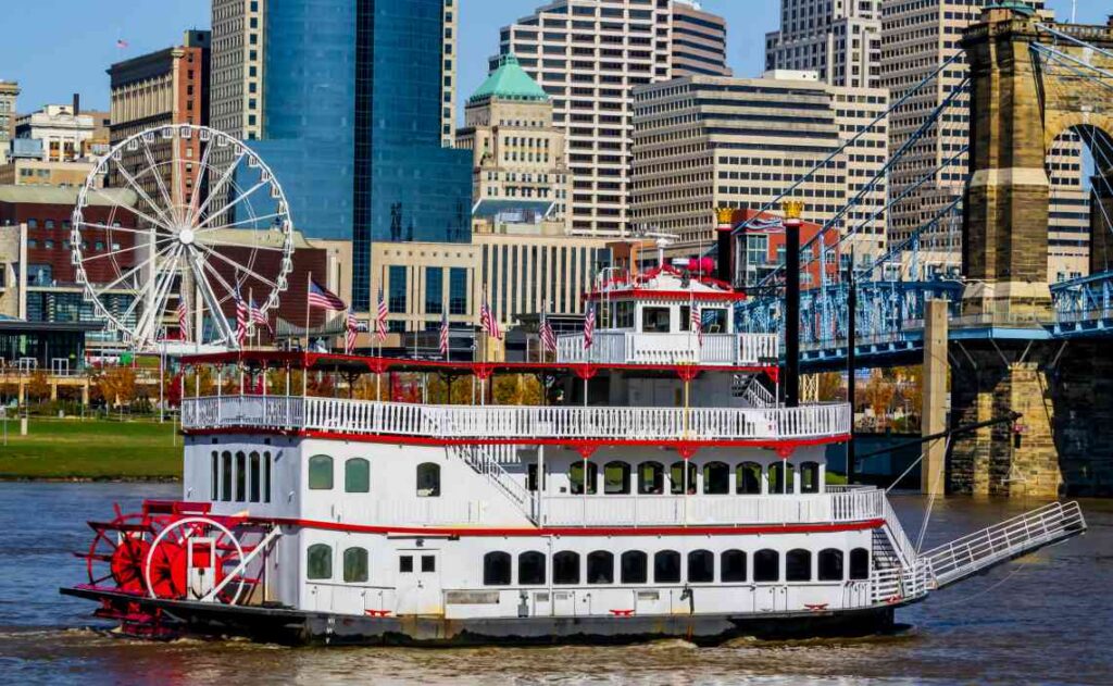 white and red riverboat on the river with downtown cincinnati in the background