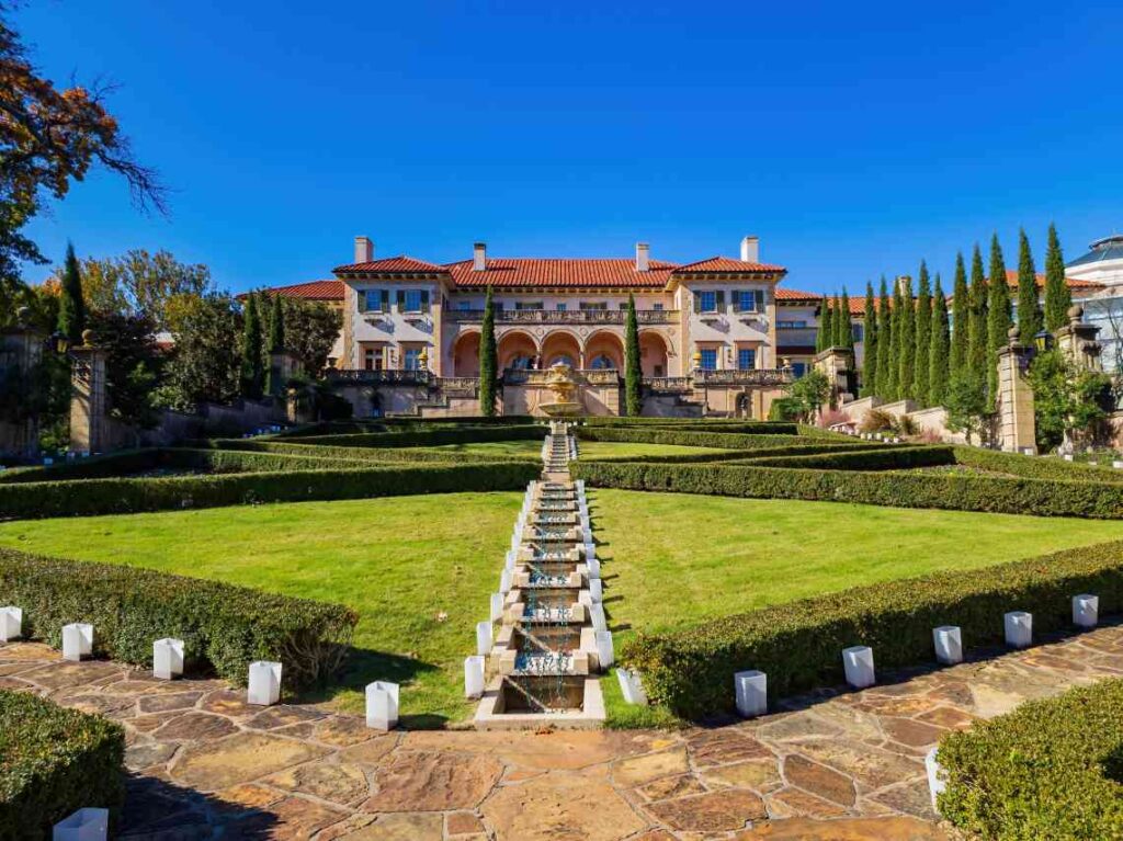 ornate villa housing the philbrook museum of art with red tile roof behind a lawn with sculpted hedges and trees