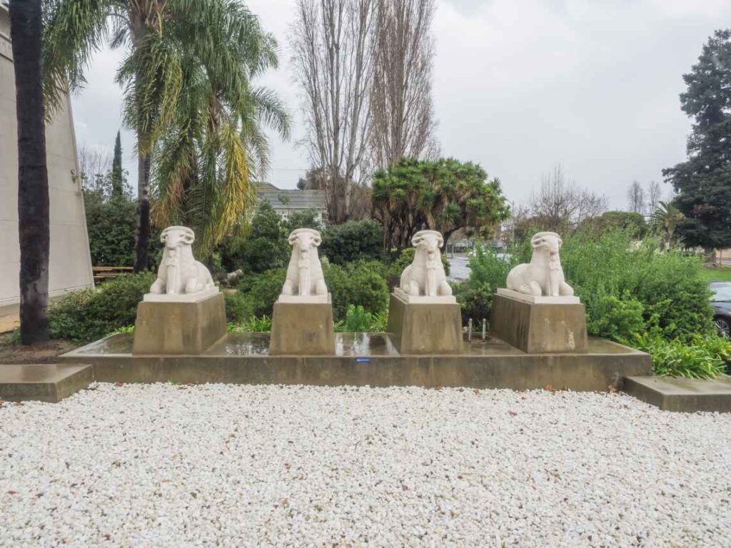 four white stone ram statues on cement pillars sitting in front of white rocks in the garden of the rosicrucian egyptian museum