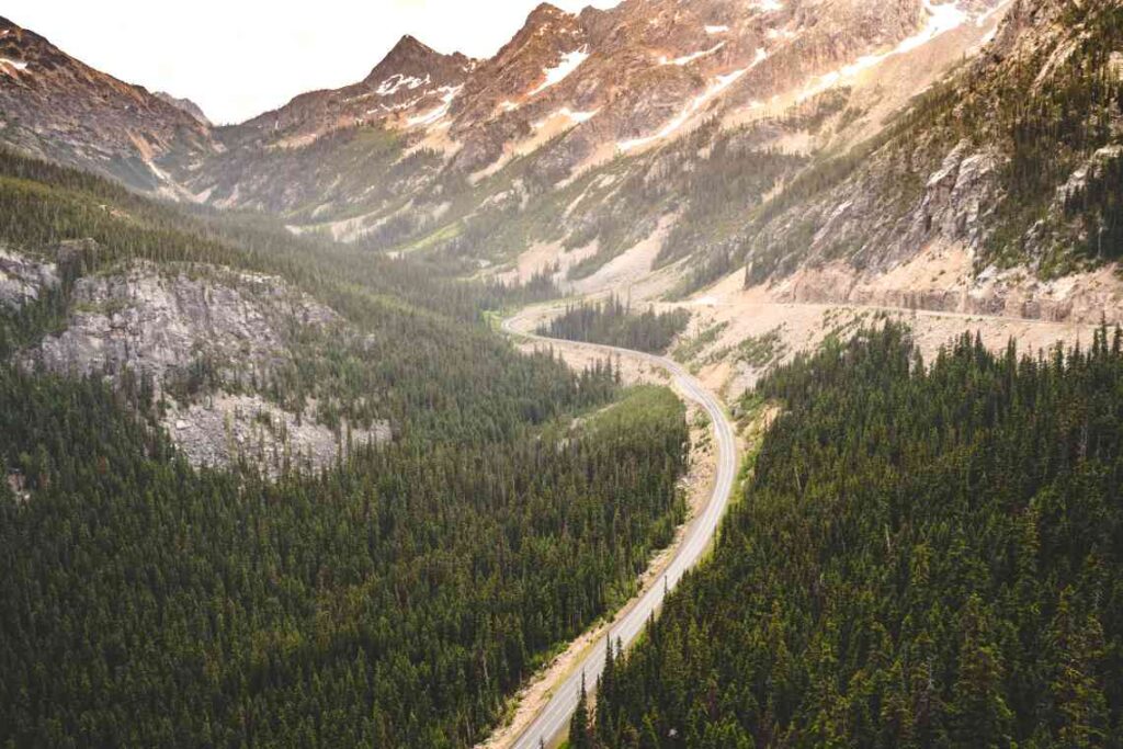 drone view of north cascades scenic byway going between mountains with green pine trees on either side