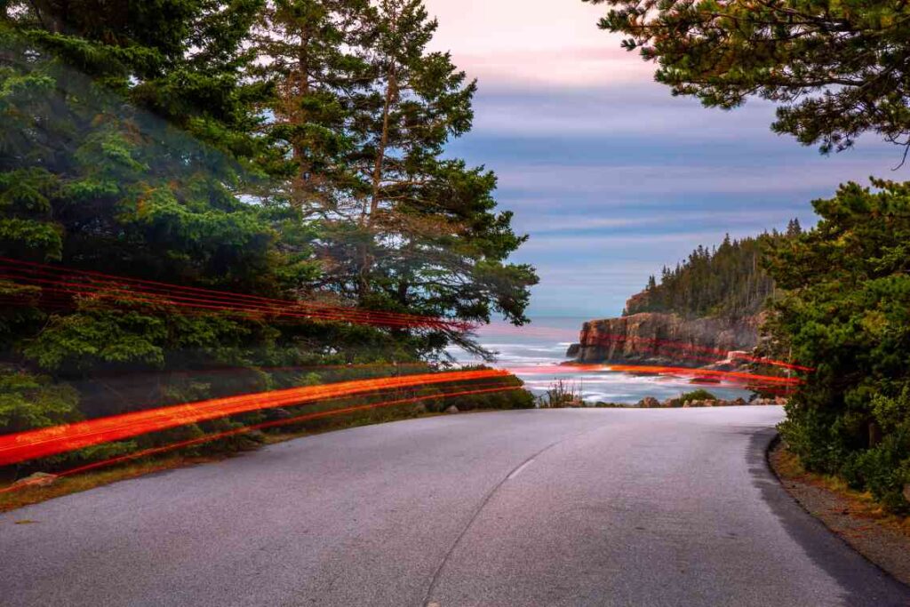 portion of park loop road in maine's acadia national park at dusk with ocean, trees and brown cliffs