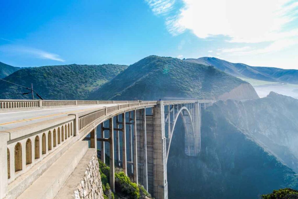 old stone bixby bridge above a canyon along the pacific coast highway with misty mountains and sunshine