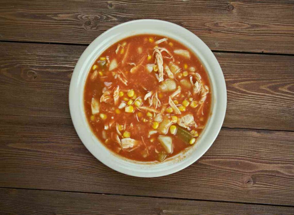 White bowl with brunswick stew, with chicken, corn, potatoes and okra, on a wood table