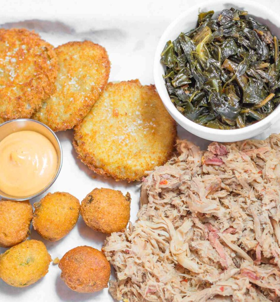 plate with chopped pork, collard greens and hushpuppies with fried green tomatoes