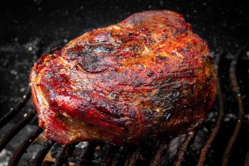 close up of browned pork shoulder cooking on a grill over coals