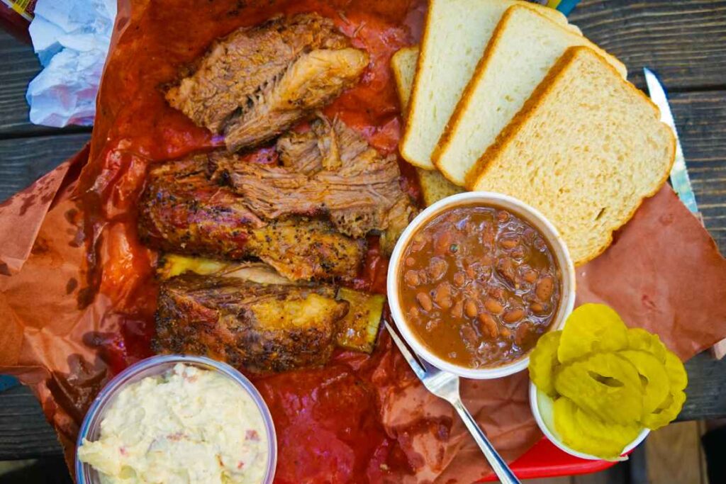 sliced brisket, beans and potato salad with white bread and pickles on a paper lined tray in austin texas
