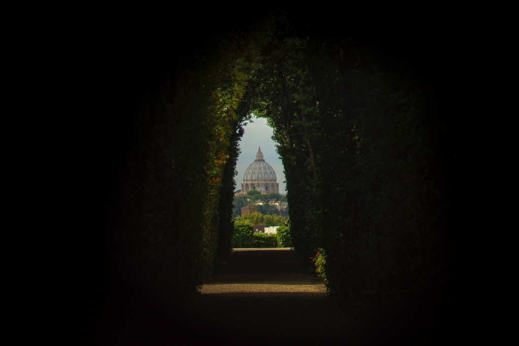 cupola of basilica from afar shot through tunnel covered in green vines