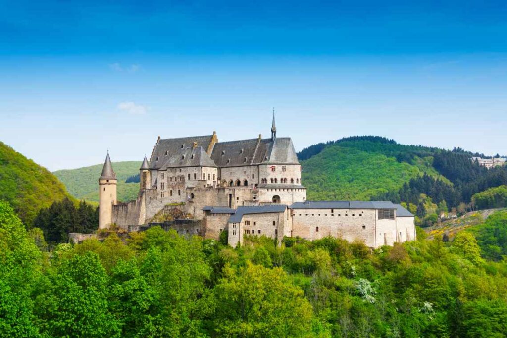 stone castle with turrets on top of a hill surrounded by green trees in luxembourg