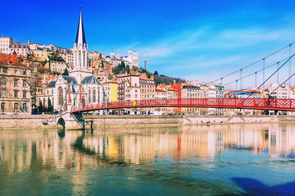 red pedestrian bridge over a river with houses and church on the other side