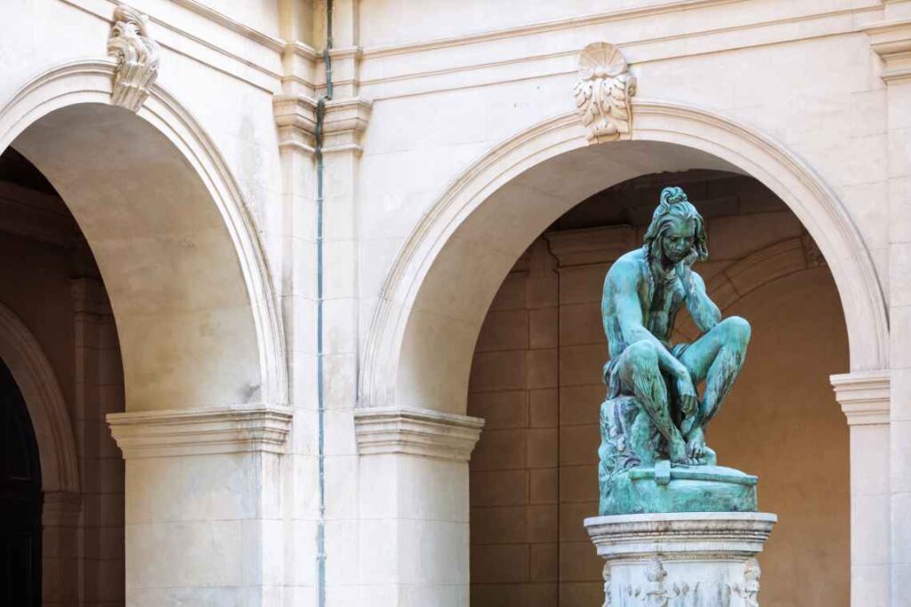 green statue of a person sitting outside the stone arches of the museum of fine arts in lyon france