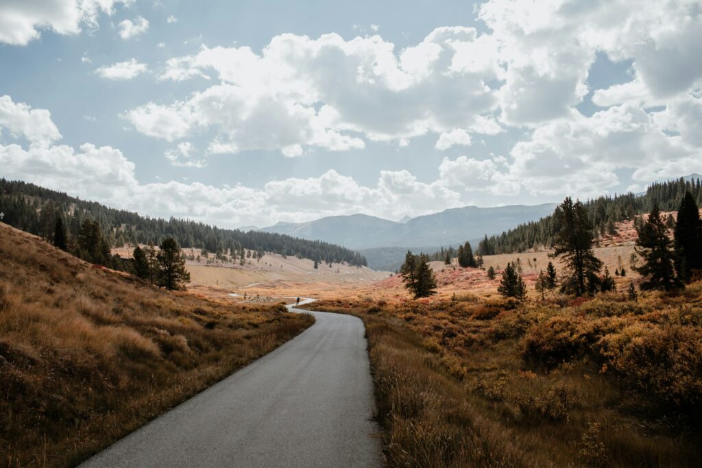 Narrow asphalt road winding through a golden valley under a partly cloudy sky.