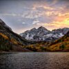 Mountain lake at sunset, surrounded by autumn foliage and rocky peaks.