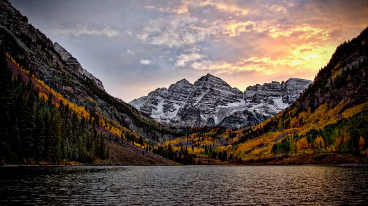 Mountain lake at sunset, surrounded by autumn foliage and rocky peaks.
