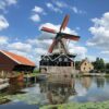 The saw windmill "De Rat" at IJlst, Netherlands, next to a calm body of water surrounded by greenery.