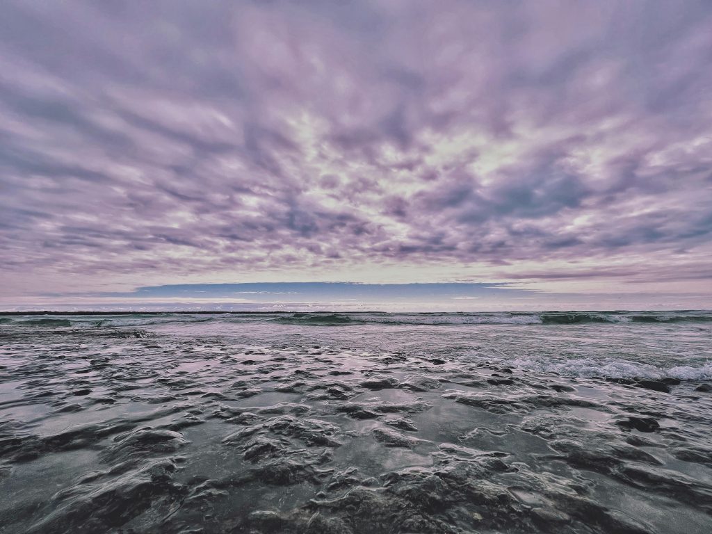 Waves washing over a rocky shoreline under a dramatic cloudy sky in Prince Edward County, Ontario.