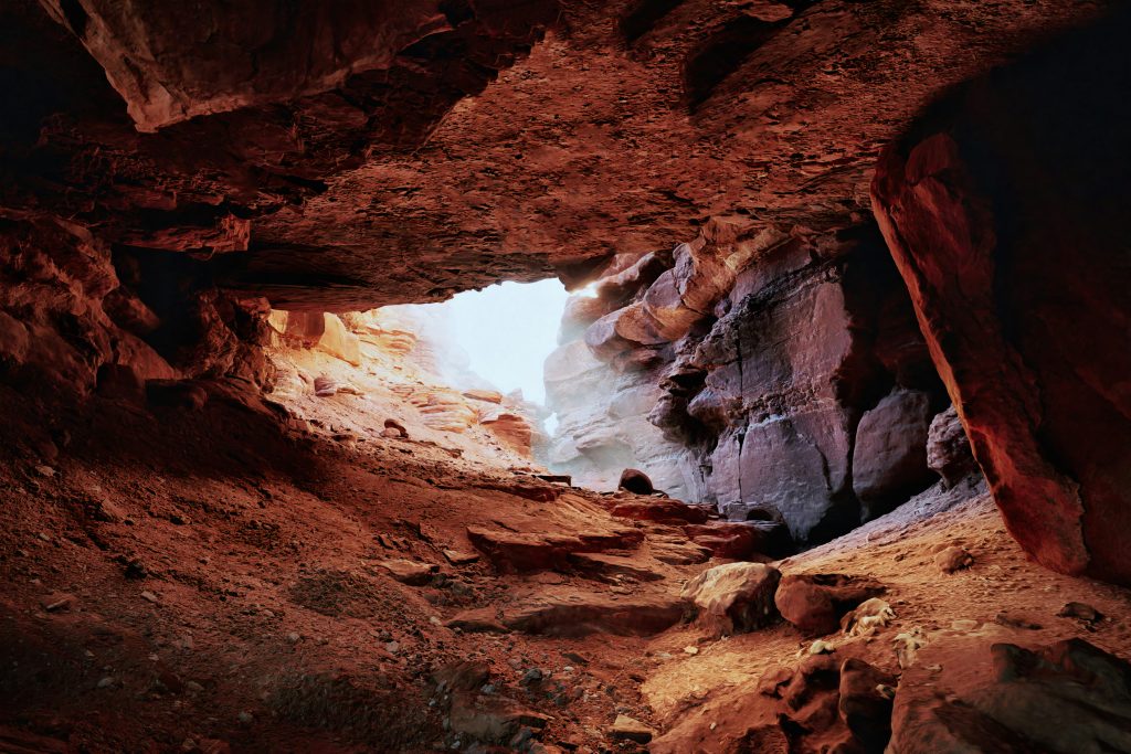 View from inside a sandstone cave looking toward a small opening letting in light.