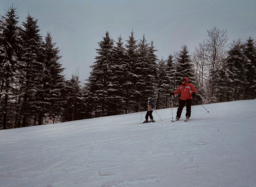 Two skiers on a snow-covered slope surrounded by pine trees at Seven Springs Mountain Resort.