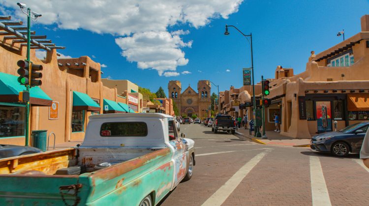 A sunny street in Santa Fe lined with adobe buildings, shops, and a vintage pickup truck.
