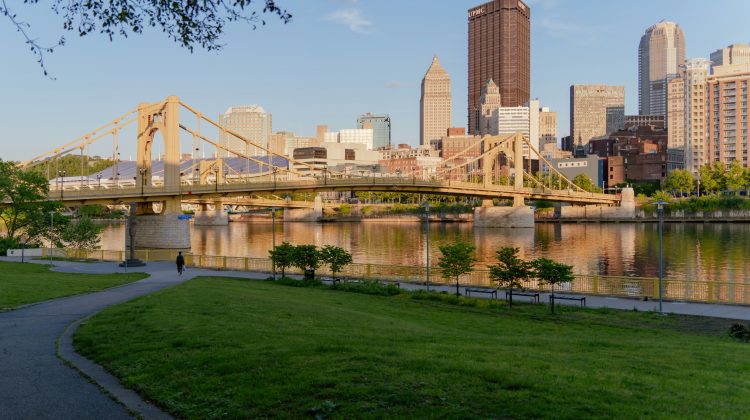 Pittsburgh's downtown skyline seen from the North Shore, with a yellow bridge crossing the Allegheny River.