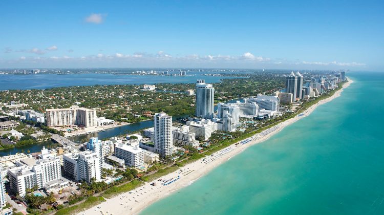 Aerial view of Miami's coastline and city buildings next to the water on a sunny day.