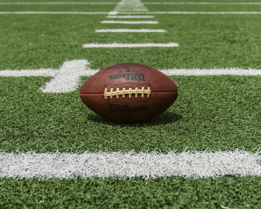 A brown Wilson football on a green football field.