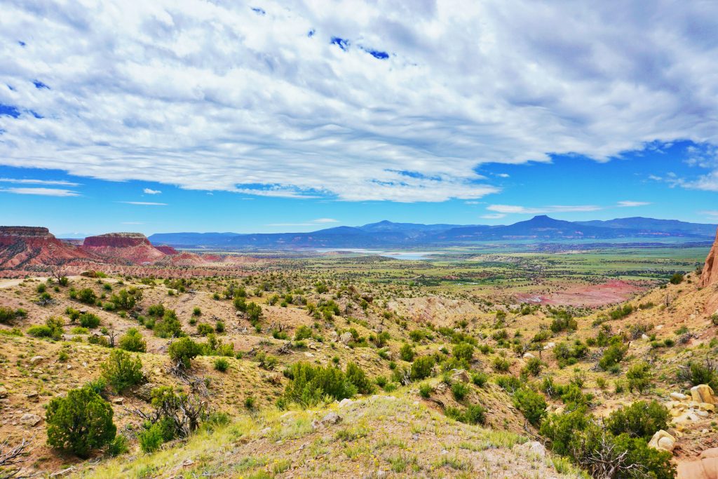 A sweeping desert landscape with red cliffs and mountains under a blue sky in New Mexico.