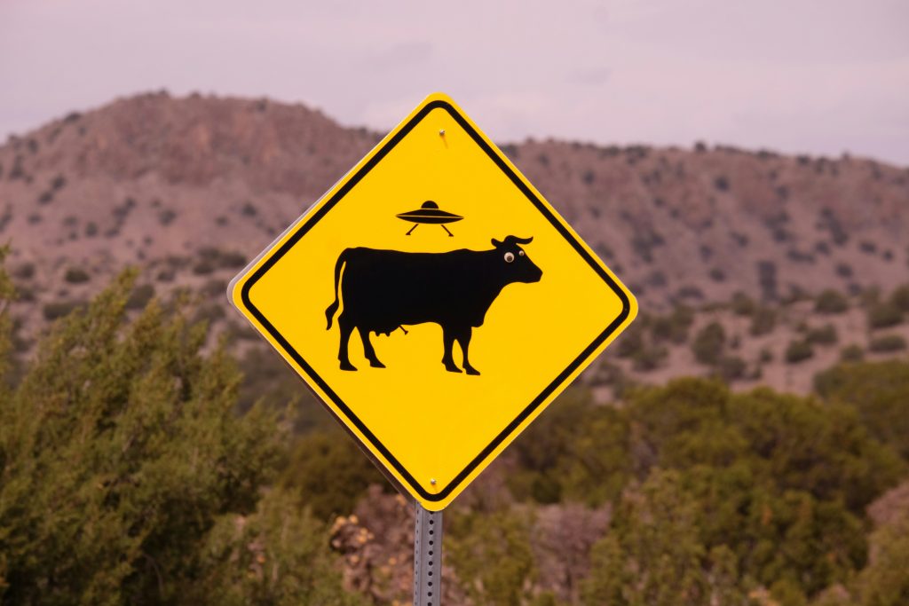 A humorous yellow road sign featuring a cow and a UFO in Madrid, New Mexico.