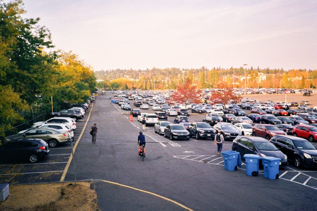 Large outdoor parking lot with rows of cars and autumn trees in the background.