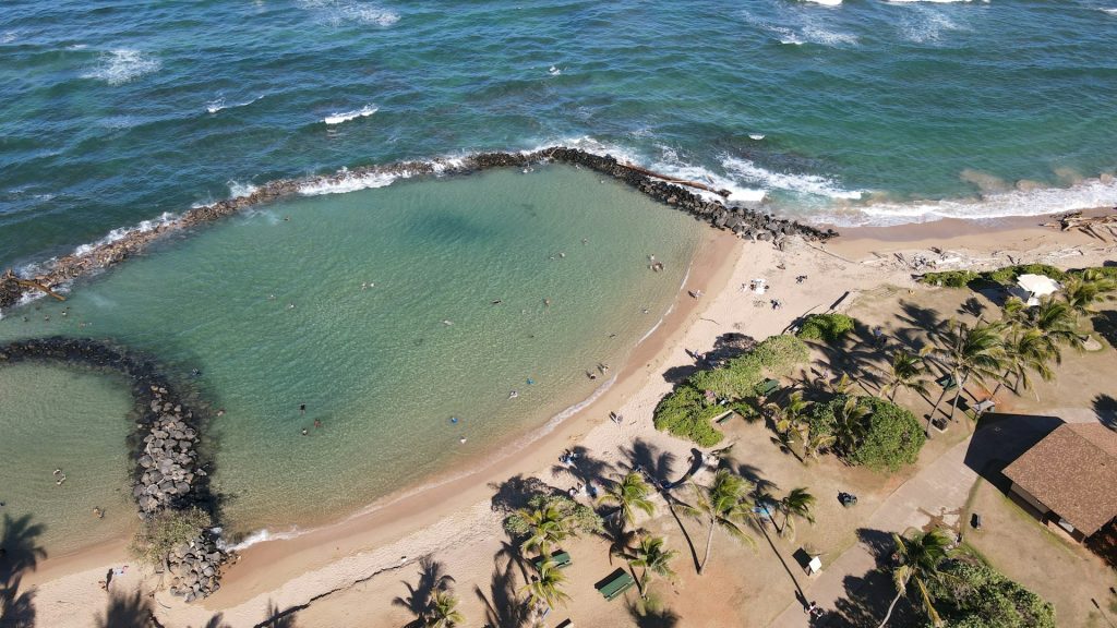 Aerial view of Lydgate Beach's rock-enclosed swimming lagoon with palm trees and sandy shore.