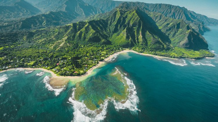 Aerial view of Kauai's dramatic coastline with turquoise waters, coral reefs, sandy beaches and lush green mountains.