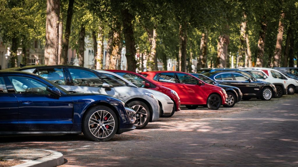 Row of colorful cars parked in an outdoor lot under shaded trees.