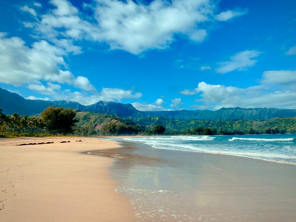 Sandy beach with turquoise waves and lush green mountains.