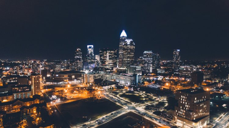 Aerial night view of Charlotte's Uptown skyline with illuminated skyscrapers and city streets.